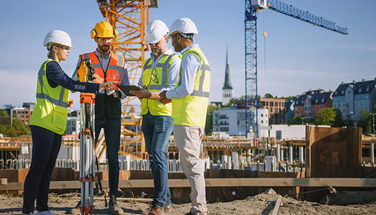 Four employees on a construction site talking together while looking at a tablet 
