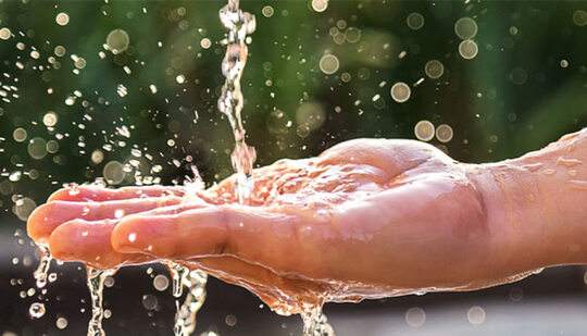 A hand onto which water is poured, causing splashes and droplets of water. 
