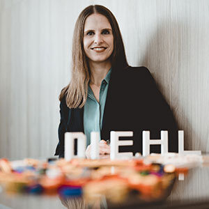 The photo of a woman facing us, smiling, with the letters DIEHL in front of her on a table. This woman is Lena Yoshihara-Lisch Chief Expert Innovation Management at Dieh Metering as well as member of Executive Board of the mioty Alliance